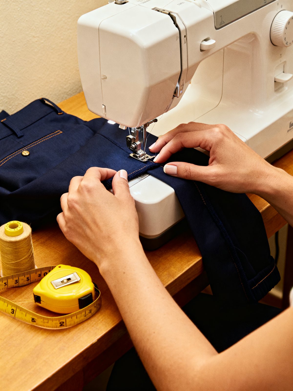 Imagen de ambiente: manos guiando el bajo de un pantalón bajo la aguja de una máquina de coser